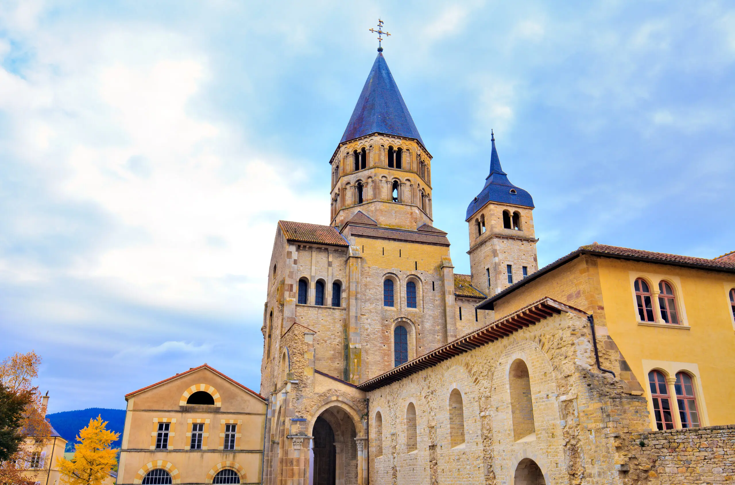 Cluny Abbey in Burgundy, France Cluny Abbey’s stone bell towers and arched windows beneath a cloudy blue sky in Burgundy, France.